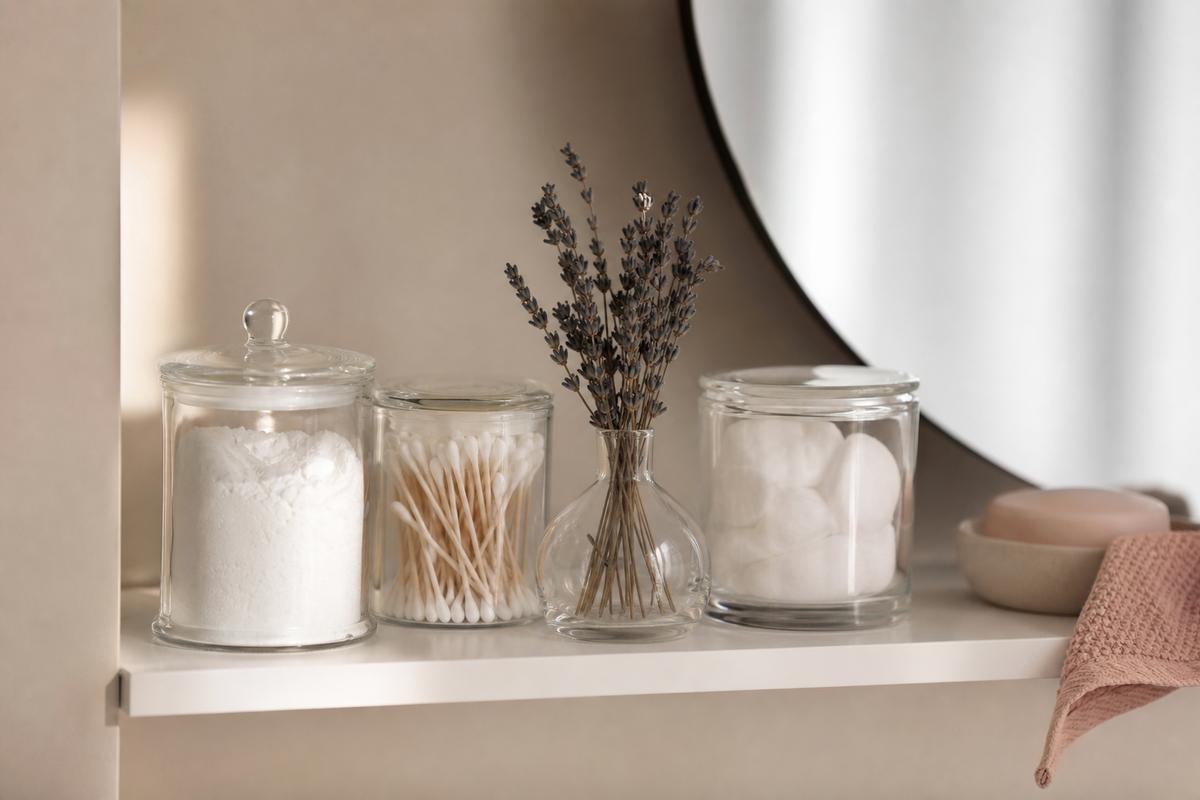 Pots en verre de bicarbonate et lavande séchée rangés sur une étagère blanche, salle de bain naturelle et épurée