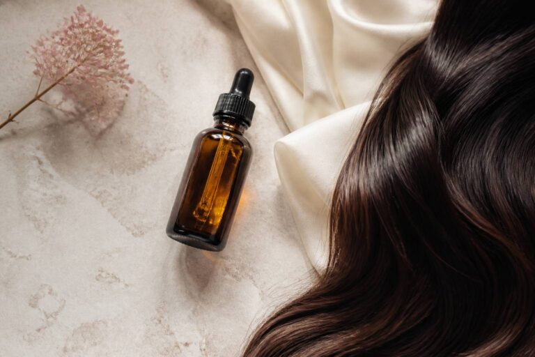 Flacon de sérum capillaire en verre ambré avec des cheveux brillants sur drap ivoire